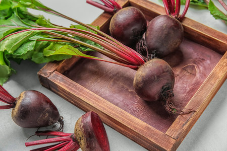Wooden board of fresh beets with green leaves on light background