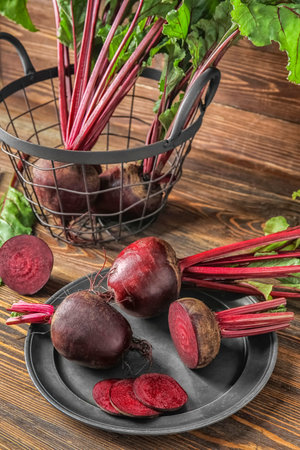 Plate and basket of fresh beets with green leaves on wooden backgroundの写真素材