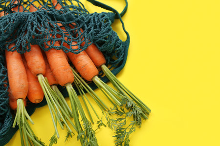 String bag with fresh carrots on yellow backgroundの写真素材