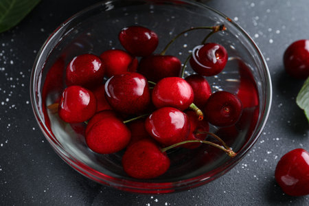 Glass bowl with sweet cherry on black background