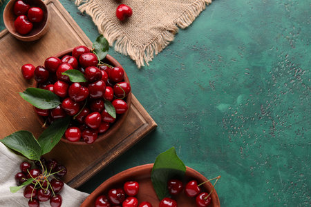 Bowls and board with sweet cherries on green backgroundの写真素材