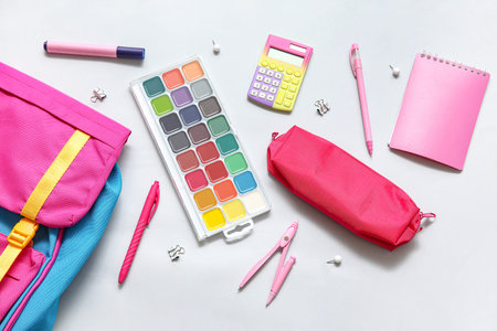 Colorful school backpack with watercolors, calculator and pencil case on white background