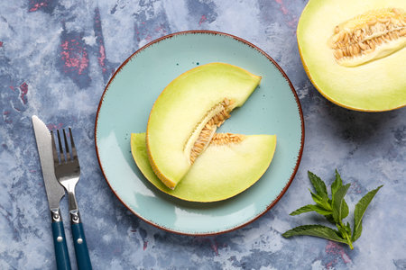 Half of sweet melon and plate with pieces on blue backgroundの写真素材