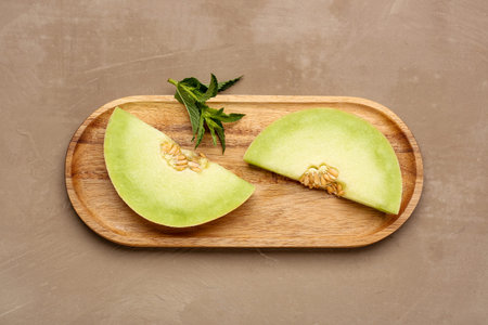 Wooden board with pieces of sweet melon and mint on brown background
