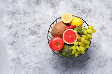 Basket with different fresh fruits and vegetables on gray backgroundの写真素材