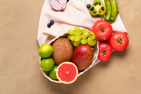 Wicker bowl with different fresh fruits and vegetables on brown backgroundの写真素材
