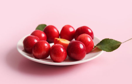 Plate with sweet cherry and leaves on pink background