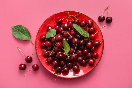 Plate of sweet cherries and leaves on pink backgroundの写真素材