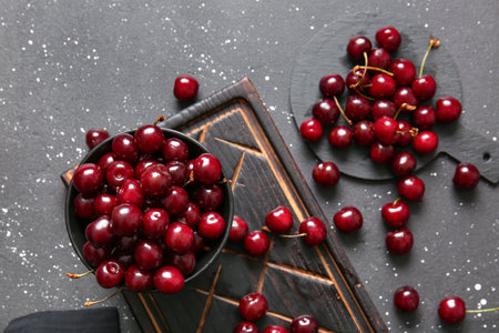 Bowl and board with sweet cherries on black tableの写真素材