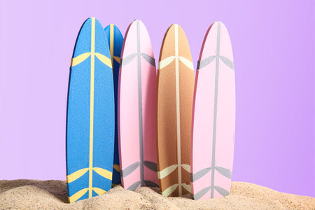 Different mini surfboards on sand against lilac backgroundの写真素材