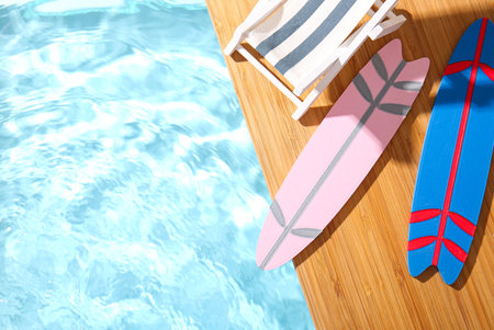 Creative composition with mini surfboards and deckchair on edge of swimming poolの写真素材