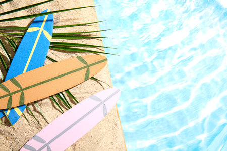 Different mini surfboards with palm leaf on sand near waterの写真素材