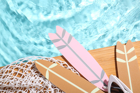 Composition with mini surfboards, net and sunglasses on edge of swimming pool