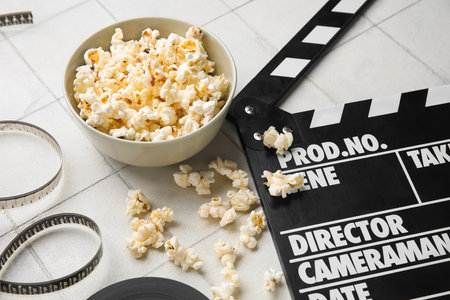 Bowl with tasty popcorn, clapperboard and film reel on white tile backgroundの写真素材