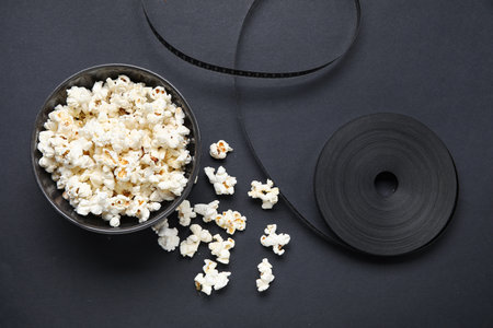 Bowl with tasty popcorn and film reel on black backgroundの写真素材