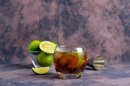 Glass of cold Cuba Libre cocktail and bowl with limes on purple backgroundの写真素材