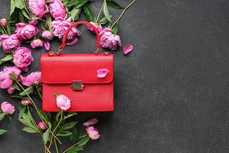 Composition with stylish female bag and beautiful peony flowers on dark backgroundの写真素材