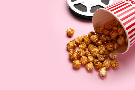 Bucket with tasty popcorn and film reel on pink backgroundの写真素材