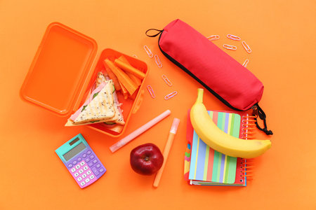 Different stationery and lunch box with tasty food on orange backgroundの写真素材