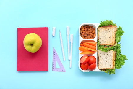 Stationery and lunch box with tasty food on blue backgroundの写真素材