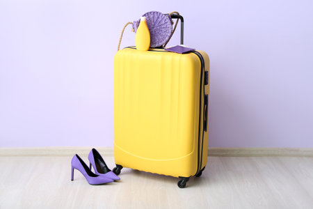 Suitcase with passport, sunscreen cream and high heels near lilac wall. travel conceptの写真素材