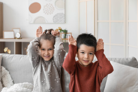 Cute little children in knitted sweaters sitting on sofa at homeの写真素材