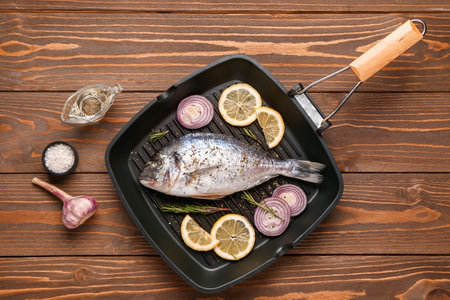 Grill pan of raw dorado fish with lemon and onion on wooden backgroundの写真素材