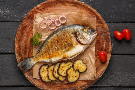 Plate with tasty grilled dorado fish on dark wooden background