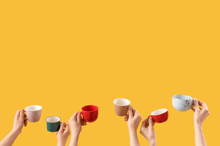 Female hands holding cups on yellow backgroundの写真素材