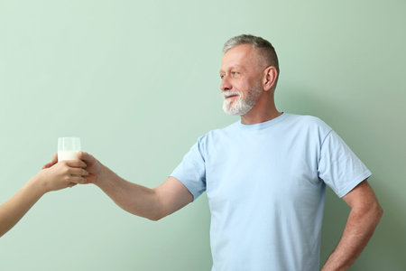 Mature man taking glass of milk on green backgroundの写真素材