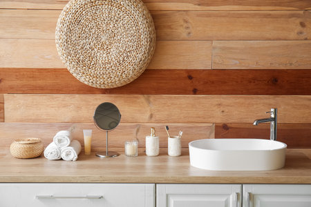 White sink with bath accessories on table near wooden wallの写真素材