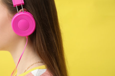 Young woman in headphones listening to music on yellow backgroundの写真素材