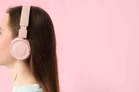 Young woman in headphones listening to music on pink backgroundの写真素材