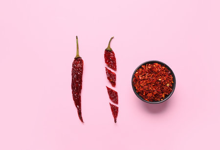 Cut chili with bowl of ground peppers on pink backgroundの写真素材