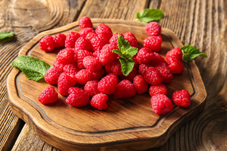 Board with fresh raspberries and mint on wooden background