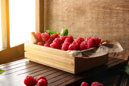 Wooden box with fresh raspberries on windowsill