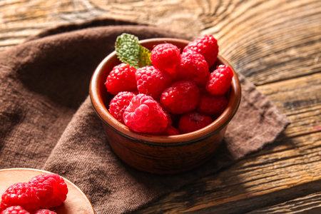 Bowl with fresh raspberries and mint on wooden background