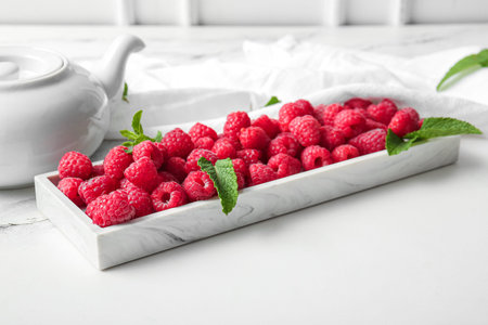 Tray with fresh raspberries and mint on white background