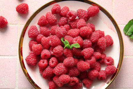Plate with fresh raspberries and mint on pink tile background