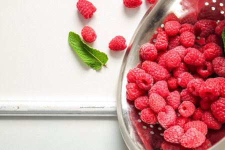 Colander with fresh raspberries and mint on white backgroundの写真素材