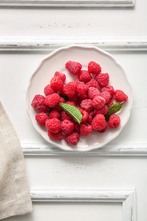 Plate with fresh raspberries and mint on white background