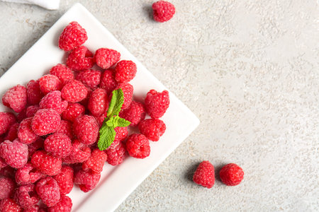 Plate with fresh raspberries and mint on gray background
