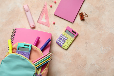 Colorful school backpack with calculators, markers and pencils on beige grunge backgroundの写真素材