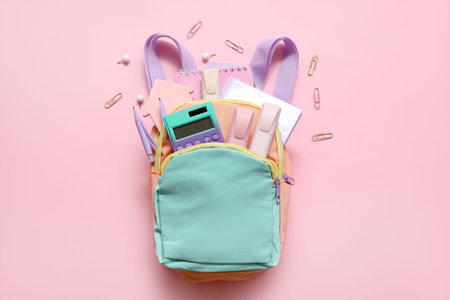 Colorful school backpack with calculator, notebooks and markers on pink background