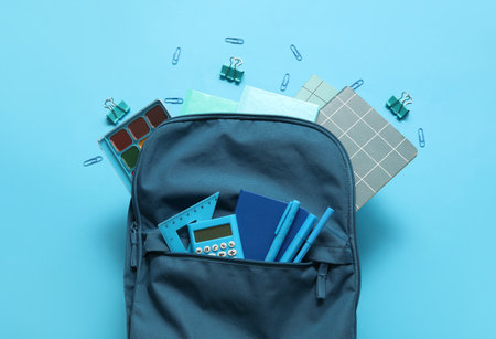 School backpack with notebooks, calculator and watercolors on blue backgroundの写真素材