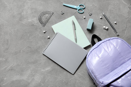 Lilac school backpack with notebooks, scissors and pens on gray grunge backgroundの写真素材