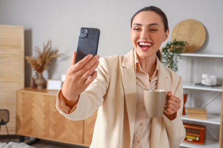 Young businesswoman with mobile phone video chatting at homeの写真素材