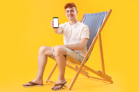 Young man with mobile phone resting in deck chair on yellow background