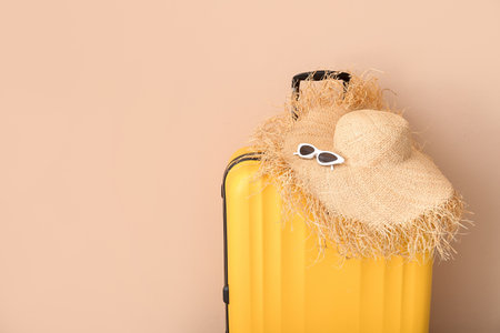 Suitcase with wicker hat and sunglasses near pale orange wall. travel conceptの写真素材