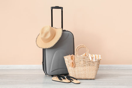 Suitcase with wicker hat, bag and beach accessories near pale orange wall. travel conceptの写真素材